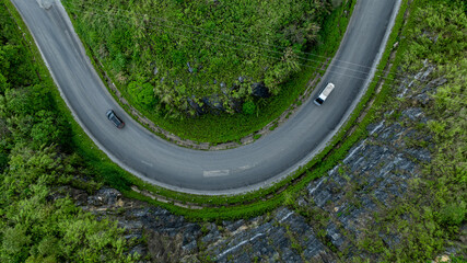 Wall Mural - Aerial view road through the green forest on mountain road, Car drive on asphalt road going through green forest, Curved road from above.