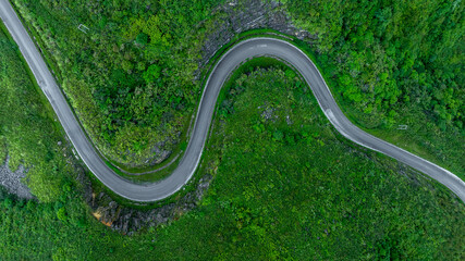 Wall Mural - Aerial view road through the green forest on mountain road, Car drive on asphalt road going through green forest, Curved road from above.