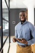 © Wavebreak Media - Holding tablet, smiling confidently, African American male professional in modern office