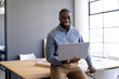 © Wavebreak Media - Smiling businessman holding laptop while sitting on desk in modern office