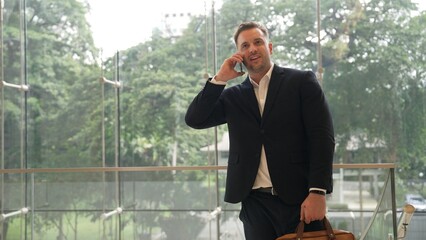 Wall Mural - Caucasian businessman calling manager by using smart phone and discuss about financial report. Male leader talking marketing team by using telephone while standing at stair in modern building. Urbane.