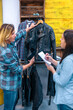 © David Pereiras - Female partners checking apparel inventory to sell in local store. Woman entrepreneur holding black leather jacket model on vintage clothes shop. Businesswomen working together in a small business.