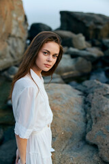 Poster - Serene young woman in flowing white dress standing on ocean rocks by the shore