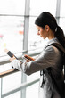 © Rabizo Anatolii - Woman holding passport, boarding pass and smartphone standing near window at airport lobby and waiting for departure. Tourist in airport is standing near panoramic window waiting for security check.