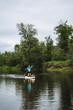 © Aleksey - A person enjoys paddle boarding on a peaceful river, surrounded by natural beauty under a serene sky, highlighting elements like water, boat, sky, paddle, lake, and trees