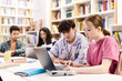 © Seventyfour - Side view portrait of young boy and girl students using laptop together at table in school library copy space