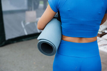 In an urban environment of asphalt, a woman in a blue shirt stands out as she strolls with a yoga mat. The electric blue hue complements her denim outfit, adding a vibrant pop of color