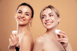 © halayalex - Beauty portrait of two amazing gorgeous beautiful blonde and brunette women. Smiling models posing naked. Female isolated over beige background. Hold jar of daily cosmetic container with facial cream