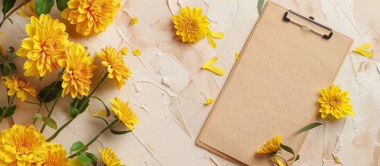 Fototapete - Top view of a beige background with a clipboard featuring a blank paper and yellow chrysanthemums, ideal for a copy space image.