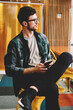 © BullRun - Young pondering skilled male employee dressed in trendy clothing planning working schedule while sitting in modern office.Pensive smart hipster guy in eyeglasses thinking about ideas for startup