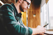 © BullRun - Cropped image of bearded male person wearing spectacles for eye protection texting email message via smartphone.Handsome talented employee solving banking issues chatting with online support indoors