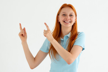 Wall Mural - Hey look. Smiling pretty female model pointing fingers left at empty space and inviting to check it out, showing advertisement on white background.