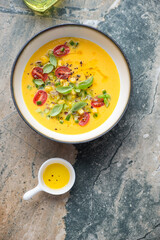 Wall Mural - Bowl of sweet corn and yellow tomatoes gazpacho, above view on a grey and beige granite background, vertical shot with space