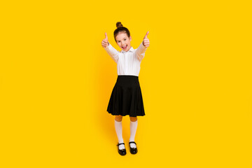 Poster - Photo of cute schoolgirl demonstrate thumb up wear uniform isolated on yellow color background