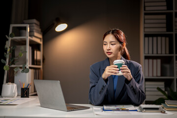 Wall Mural - A woman in a blue suit is sitting at a desk with a laptop and a cup of coffee