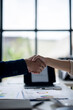 © Wasana - Two people shaking hands in front of a table with a laptop and papers