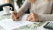 © lililia - A woman signs a document on a table covered with cash, indicating a financial transaction or agreement.