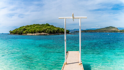 Wall Mural - A panorama view past a wooden jetty towards islands offshore from the beach at Ksamil, Albania in summertime