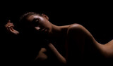This is a photo of a woman posing in silhouette against a dark background. Her body is partially visible, with her face and shoulders illuminated by a soft light.