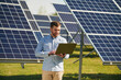 © standret - Holding laptop. Engineer with photovoltaic solar panels outdoors at daytime