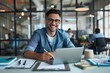 © ammad - A smiling man in glasses sitting at desk with laptop holding pen looking into camera Professional stress free Workspace Concept