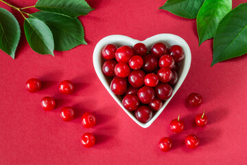 Wall Mural - Cherries in a white heart-shaped bowl on a red surface