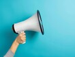 © Mahmud Creative - Female hand holding a megaphone on blue background with copy space