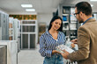 © bnenin - A female customer holding some ceramic tiles and talking to a male seller, at the home design shop.