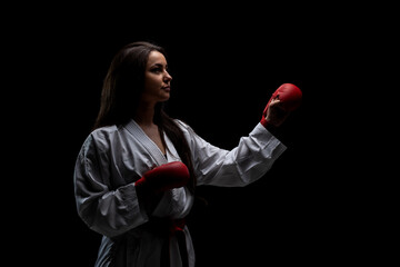 Wall Mural - girl exercising karate punch wearing kimono and red gloves against black background