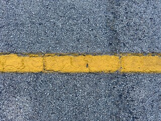 A yellow line on an asphalt road surface provides clear guidance and separation for drivers, ensuring safety and order on the roadway with its bright, unmistakable marking.