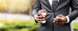© Prostock-studio - Busy businessman using smartphone browsing internet and drinking take-out coffee outdoors, closeup