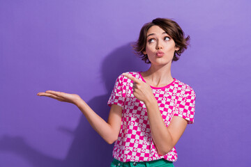 Wall Mural - Photo of cute lovely stylish girl with pouted lips looking empty space arm presenting new products isolated on purple color background