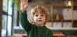 © SardarMuhammad - Curious child in a green sweater, raising hand to ask a question in a modern, minimalist classroom.