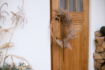 Wall Mural - Stylish modern autumn wreath on wooden doors. Fall decor of farm house entrance. Rustic wreath with dried grass, herbs and ribbon. Thanksgiving and Halloween