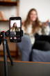 © Anatoliy Karlyuk - Selective focus on camera of smartphone standing on tripod recording podcast of female blogger or influencer gesticulating and sharing advice with subscribers or followers of her blog or vlog