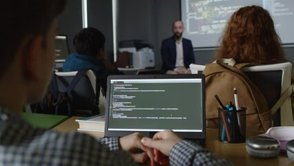medium rear shot of group of teenage school students sitting at desks with laptops with programming 