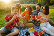 © maxbelchenko - Young cheerful friends happy positive smile eat fruit watermelon party countryside outdoors. Foods, travel, nature and picnic concept