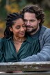 © Irina Kozel - A young black woman with braided hair and a happy Hispanic man with a beard embrace on a park bench, she in a green blouse, he in a gray sweater, with a blurred background