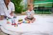© Taras Grebinets - Smiling baby playing on blanket with colorful toys outdoors