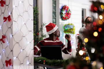 Wall Mural - Worker tasked with stressful job duties bothered by background noise made by coworkers laughing while enjoying Christmas holiday season. Employee working on laptop, surrounded by in xmas ornaments