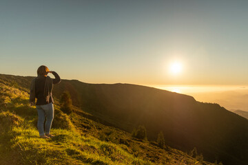 Wall Mural - Young woman watching a beautiful sunset on the mountains in Lagoa do Fogo, Sao Miguel, Azores, Portugal. Golden hour landscape.