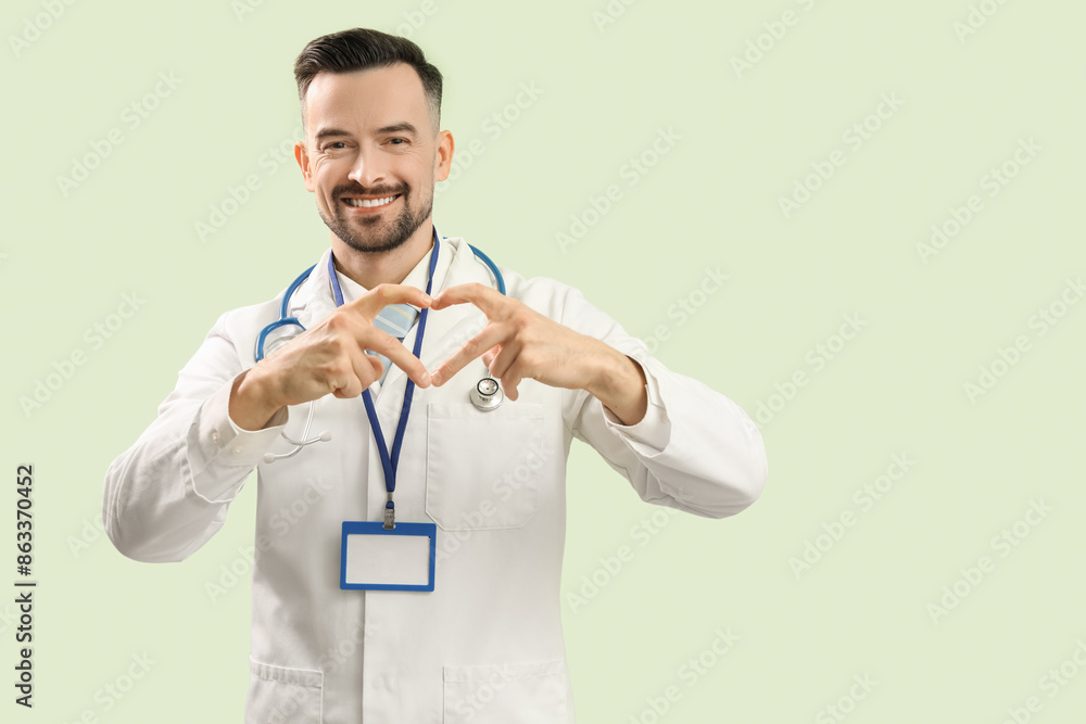 Male doctor making heart with his hands on green background