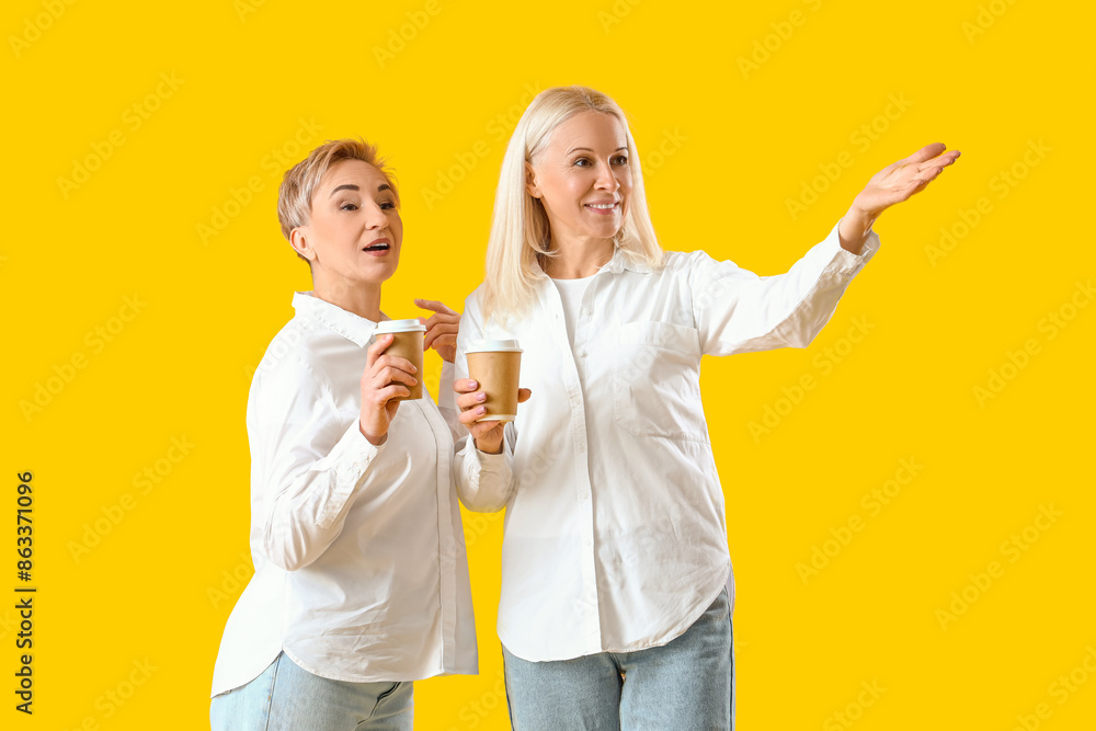 Beautiful mature women with coffee on yellow background