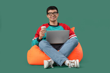 Male programmer with cup of coffee and laptop sitting on green background