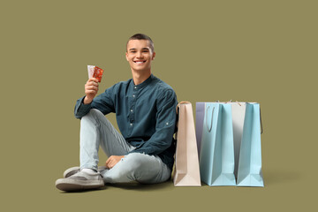 Wall Mural - Young man with gift cards and shopping bags on green background