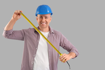 Canvas Print - Male construction worker with measuring tape on grey background