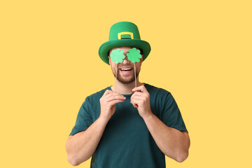 Wall Mural - Funny young man in leprechaun's hat with clovers on yellow background. St. Patrick's Day celebration