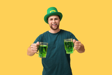 Wall Mural - Handsome young man in leprechaun's hat with mugs of beer on yellow background. St. Patrick's Day celebration