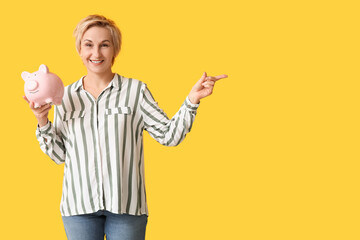 Sticker - Beautiful mature woman with piggy bank pointing at something on yellow background