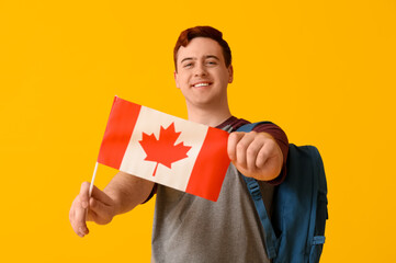 Canvas Print - Male student with flag of Canada and backpack on yellow background